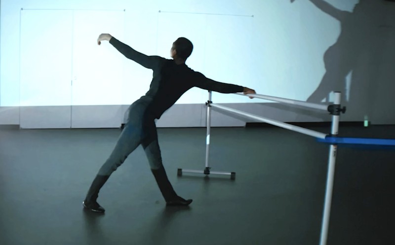 Christopher Grant dances at the barre, his shadow moving with him in the background